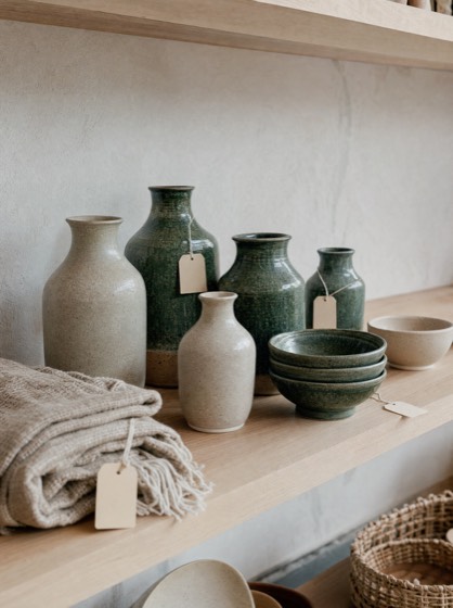 Étagère en chêne clair d'une boutique de décoration, vases et bols en grès émaillés vert et écru.